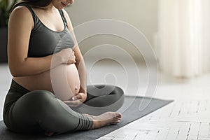 Young Pregnant Woman In Activewear Sitting On Yoga Mat And Embracing Belly