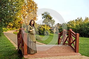 Young pregnant woman in anticipation of a baby standing in a park in the sun rays