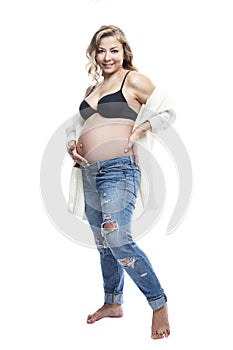 Young pregnant woman. Beautiful smiling blonde in jeans and a black bra. Love and tenderness in anticipation of the baby. Isolated