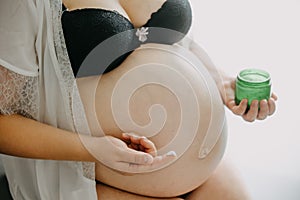 Young pregnant woman with the belly smearing cream against stretch marks, pregnancy concept