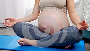 Young pregnant woman with big belly sitting on fitness mat and meditating at home. Concept of healthy lifestyle