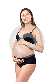 Young pregnant woman in black swimsuit. Girl expecting a baby and touching her belly isolated on white background.