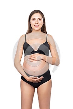 Young pregnant woman in black swimsuit. Girl expecting a baby and touching her belly isolated on white background.