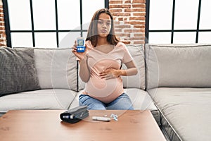 Young pregnant woman checking blood sugar looking at the camera blowing a kiss being lovely and sexy