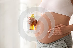 Young pregnant woman with cosmetic product in bathroom. Space for text