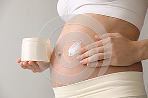 Young pregnant woman with cosmetic product on grey background, closeup