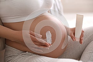 Young pregnant woman with cosmetic product indoors, closeup