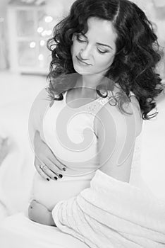 Young pregnant woman with curly long hair in a white dress by the Christmas tree. Pregnancy.