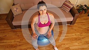 Young pregnant woman doing fitness exercises on a fitness ball. Exercises for pregnant women. Fitness at home. Closeup