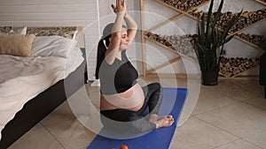 Young pregnant woman doing fitness and yoga exercises on blue mat at home.