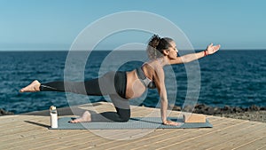 Young pregnant woman doing prenatal pilates exercises session next the sea