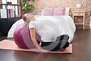 Young pregnant woman doing prepartum exercise leaning on fit ball at bedroom