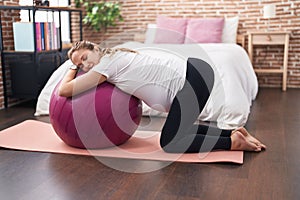 Young pregnant woman doing prepartum exercise leaning on fit ball at bedroom