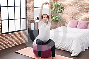 Young pregnant woman doing prepartum exercise sitting on fit ball at bedroom