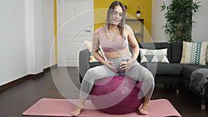 Young pregnant woman doing prepartum exercise sitting on fit ball at home