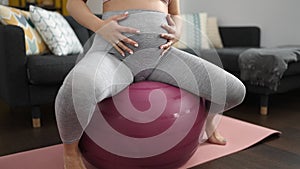 Young pregnant woman doing prepartum exercise sitting on fit ball at home
