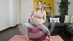 Young pregnant woman doing prepartum exercise sitting on fit ball at home