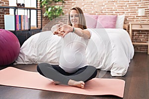 Young pregnant woman doing prepartum exercise sitting on yoga mat at bedroom