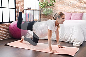 Young pregnant woman doing prepartum exercise sitting on yoga mat at bedroom