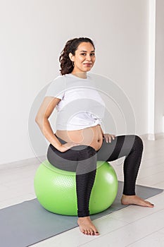 A young pregnant woman doing relaxation exercise using a fitness ball while sitting on a mat.