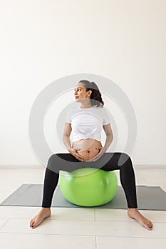 A young pregnant woman doing relaxation exercise using a fitness ball while sitting on a mat.