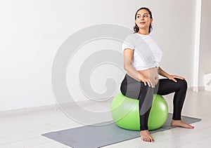 A young pregnant woman doing relaxation exercise using a fitness ball while sitting on a mat. Copyspace