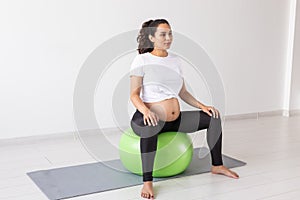 A young pregnant woman doing relaxation exercise using a fitness ball while sitting on a mat. Copyspace