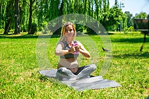 Young pregnant woman doing sport exercises on green grass in the park.