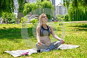 Young pregnant woman doing sport exercises on green grass in the park.