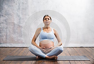 Young pregnant woman doing yoga exercises and meditating at home. Health care, mindfulness, relaxation and wellness