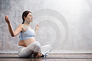 Young pregnant woman doing yoga exercises and meditating at home. Health care, mindfulness, relaxation and wellness