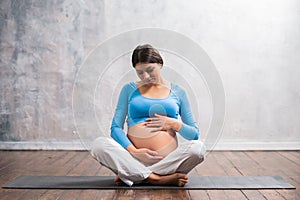 Young pregnant woman doing yoga exercises and meditating at home. Health care, mindfulness, relaxation and wellness