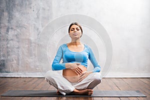 Young pregnant woman doing yoga exercises and meditating at home. Health care, mindfulness, relaxation and wellness