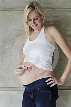 Young pregnant woman drawing a lipstick heart on belly