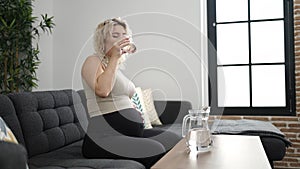 Young pregnant woman drinking glass of water sitting on sofa at home