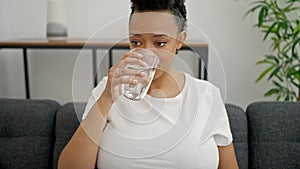 Young pregnant woman drinking glass of water sitting on sofa at home