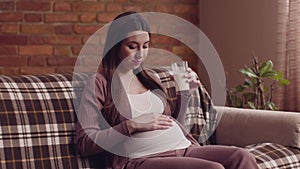 Young pregnant woman drinking milk, resting on couch at home, filling the calcium deficit