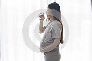 Young pregnant woman drinking water at home, healthcare and pregnancy care concept