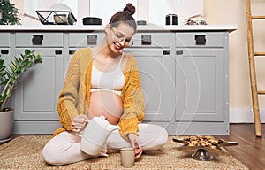 A young pregnant woman drinks tea on the kitchen floor