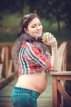 Young pregnant woman eating apple in nature