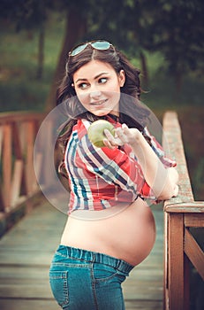 Young pregnant woman eating apple in nature