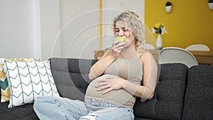 Young pregnant woman eating apple touching belly at home