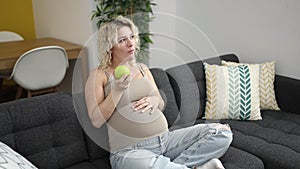 Young pregnant woman eating apple touching belly at home