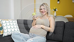 Young pregnant woman eating apple touching belly at home