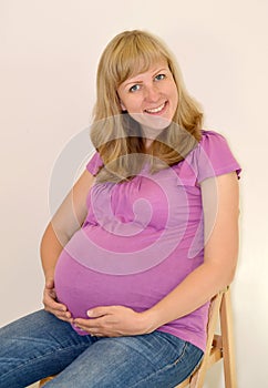 The young pregnant woman embraces hands a stomach on light a background