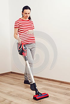 Young pregnant woman enjoys cleaning her house. Easy cleaning with a wireless vacuum cleaner