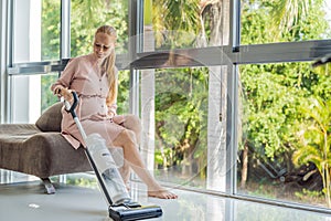 Young pregnant woman enjoys cleaning her house. Easy cleaning with a wireless vacuum cleaner. Pregnant woman cleaning