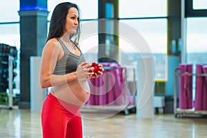 Young pregnant woman exercising knee-bending with dumbbells in gym.