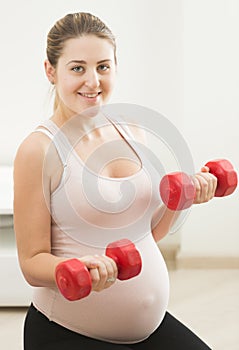 Young pregnant woman exercising with weights at home