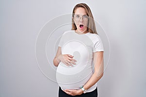 Young pregnant woman expecting a baby, touching pregnant belly afraid and shocked with surprise and amazed expression, fear and
